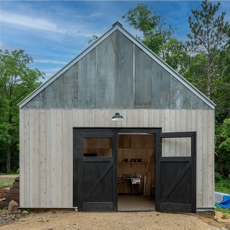 Black Z-brace carriage garage doors installed on a modern barn-style building with light wood siding and a metal gabled roof in daylight.