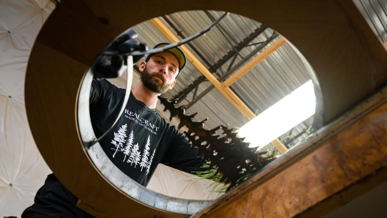 A woodworker installing an art piece in the window of a round top door, view from the bottom up through the window hole, with the art and woodworker in view.